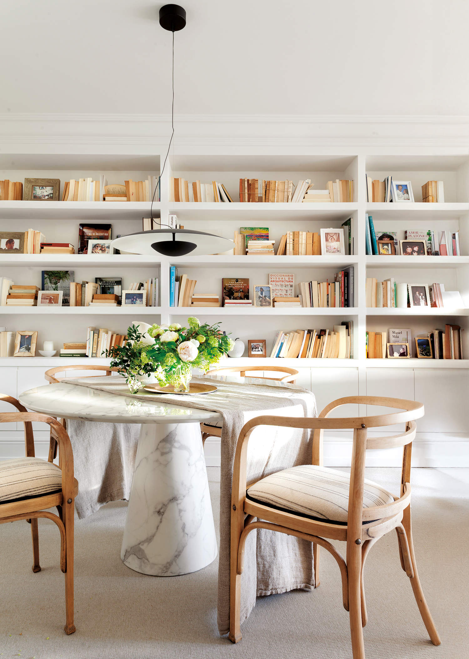 Mesa de comedor cálida con mesa redonda de mármol y librería a medida atrás